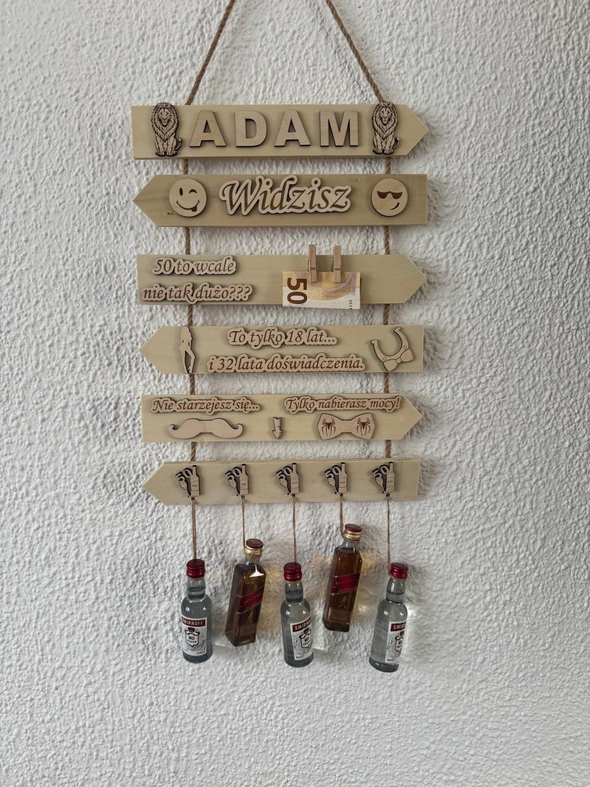 Houten wandbord met naam, humoristische teksten en hangende miniflesjes voor een 50e verjaardag
