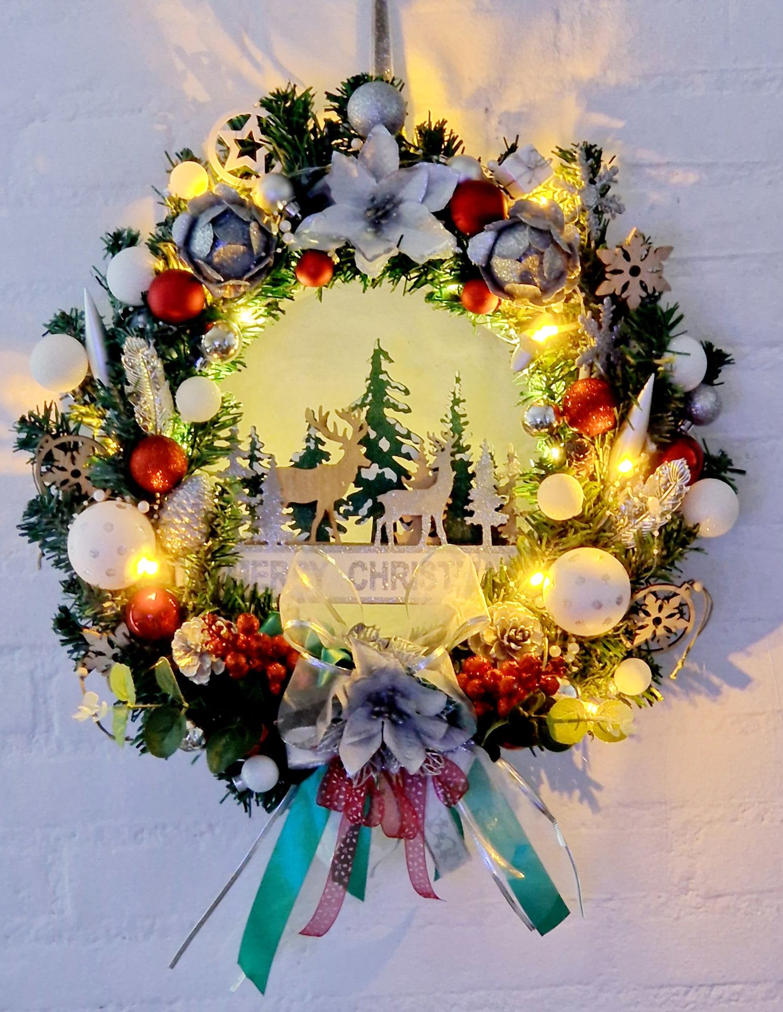 Verlichte kerstkrans met herten, dennengroen en linten