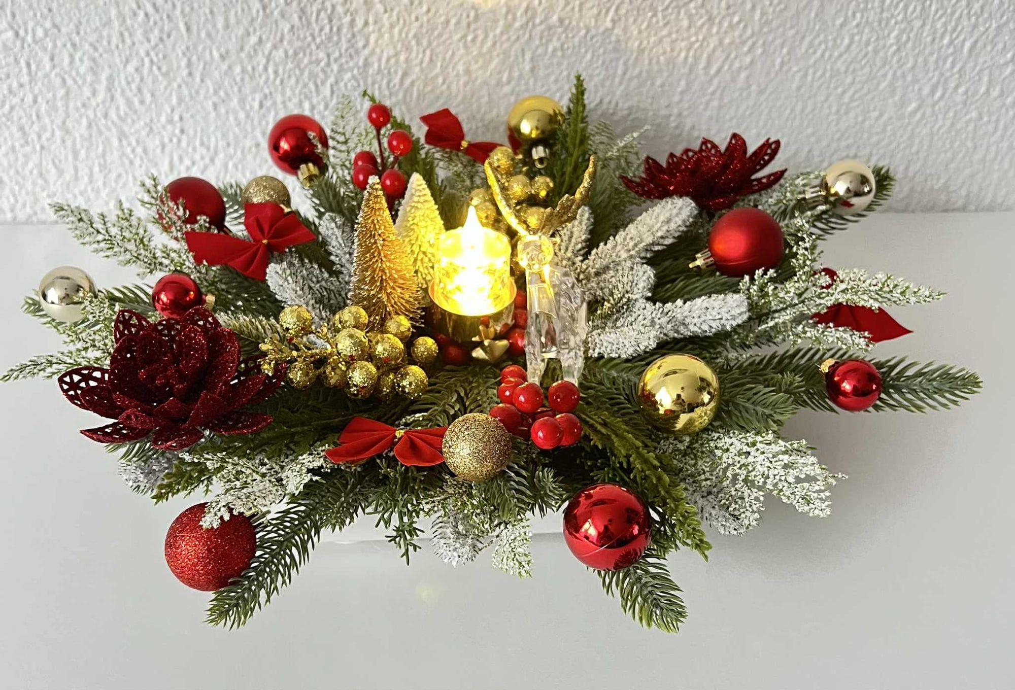 Kersttafelstuk met ledkaars, rode en gouden kerstballen en besneeuwd groen